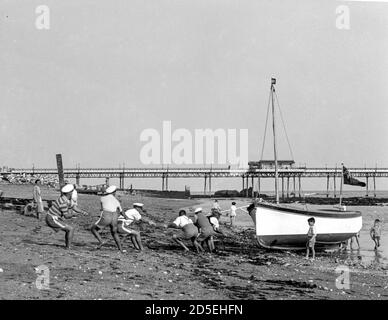Un groupe d'hommes transportent leur bateau jusqu'à la plage et hors de la mer à Shanklin, île de Wight dans les années 1950 Banque D'Images