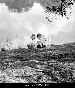 Deux jeunes enfants, frère et sœur, jouent sur le bord de la rivière ou du lac dans les années 1950 Banque D'Images