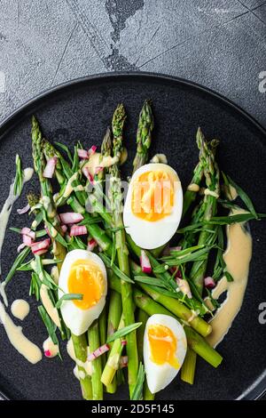 Asperges avec œufs et vinaigrette française avec moutarde de dijon, oignon haché dans de l'estragon au vinaigre rouge sur fond texturé gris, vue du dessus. Banque D'Images