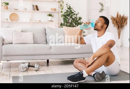 Black Man Drinking Water pendant l'entraînement assis sur le tapis à l'intérieur Banque D'Images