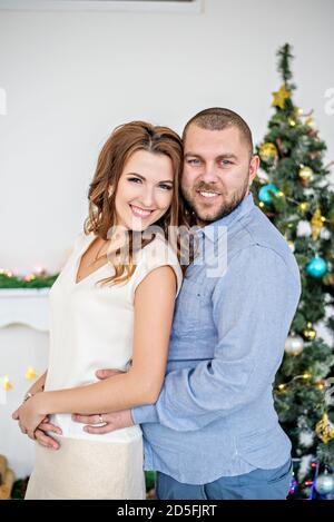 Portrait rapproché d'un couple amoureux sur fond de bokeh d'un arbre de Noël. Un jeune homme avec une barbe encadre une belle femme dans un Banque D'Images