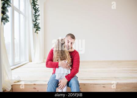 Un portrait en gros plan d'un père heureux et d'une petite fille sur un fond blanc de bokeh jaune. Un jeune homme avec une barbe joue et épouse sa fille. Banque D'Images