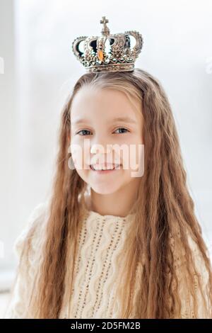 Portrait rapproché d'une petite fille blonde une robe pull blanc avec une couronne sur sa tête. Elle sourit et regarde dans la caméra. La Reine des neiges Banque D'Images