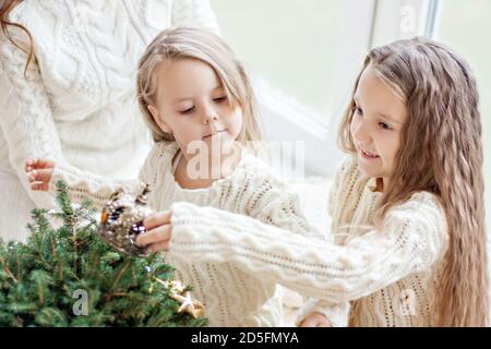 Deux amies de la sœur blonde en chandails blancs tricotés Et les chaussettes jouent par la fenêtre panoramique avec Noël arbres en prévision Banque D'Images