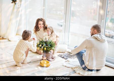 Une belle famille de jeunes couples et leurs deux filles s'amusent à célébrer le nouvel an. Arbre de Noël dans une casserole, grande fenêtre panoramique et festi Banque D'Images