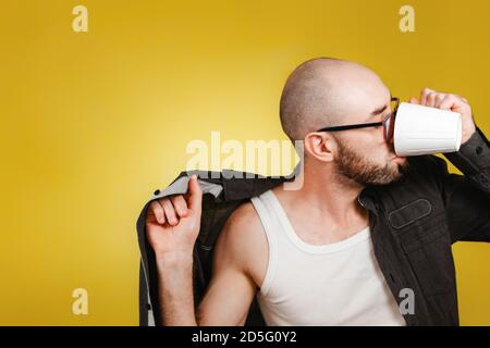 Le concept de réveil et de productivité du matin. Un homme à barbe chauve portant des lunettes, portant une chemise et buvant du café ou du thé d'une tasse au s Banque D'Images