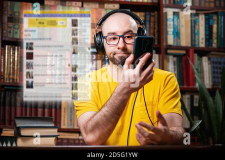 Réseau social. Un homme chauve et attentionné avec des lunettes et des écouteurs utilise un smartphone. Fenêtre transparente numérique au-dessus du téléphone. Le concept de faux Banque D'Images