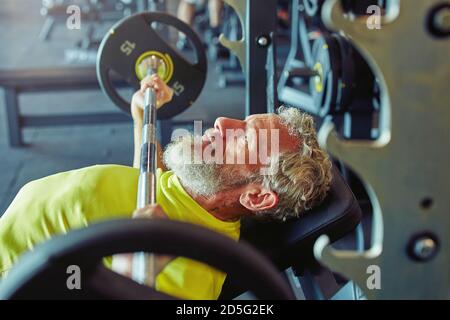 Repousser les limites du corps humain. Vue latérale d'un homme caucasien mature qui lève un bar ou une barbell à la salle de sport Banque D'Images