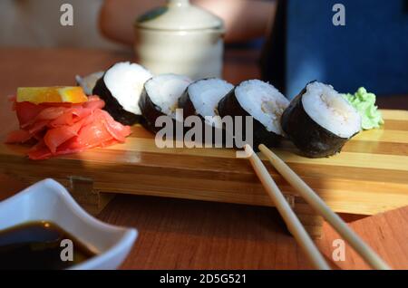 Petits pains au saumon et au caviar servis sur une assiette de petits pains à sushis sur une table dans un restaurant sur un stand en bois avec des baguettes. Sauce soja, gingembre rouge et Banque D'Images