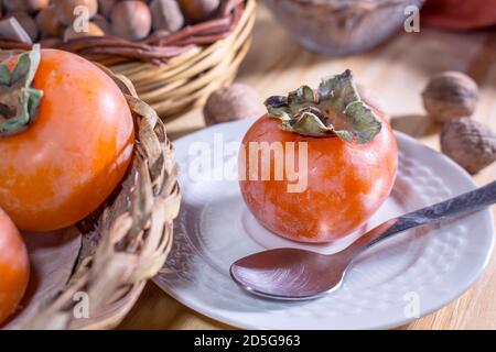 Un petit persimmon sur une soucoupe avec des cupules. En arrière-plan paniers en osier avec d'autres persimmons et fruits secs Banque D'Images