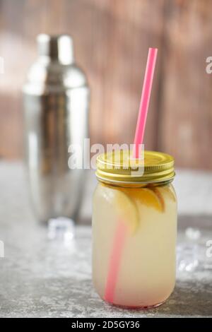 Pot rempli de boisson au citron, de menthe et de tranches de citron et d'orange, sur un sol gris entouré de plus de tranches citriques et de glace, avec un shaker de queue de cokcelle Banque D'Images