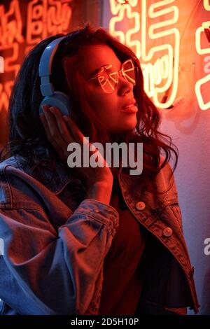 Femme afro-américaine portant un casque pour écouter de la musique avec une lumière au néon. Banque D'Images