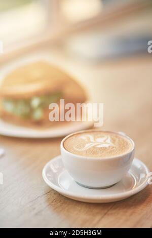 Gros plan vertical d'une tasse de café cappuccino et sandwich sur une table en bois dans le café, mise au point sélective Banque D'Images