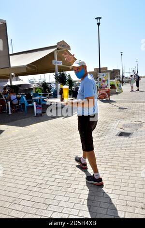 Homme portant des boissons sur le plateau tout en portant un masque facial pour covid Banque D'Images