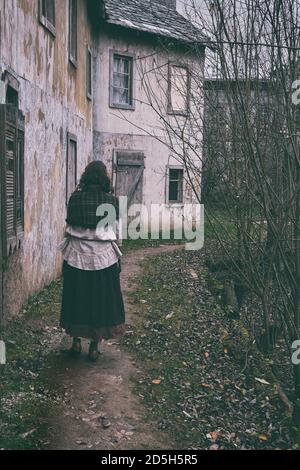 Une fille avec un châle sur ses épaules marche le long le chemin de la vieille ville sombre avec des bâtiments rétro de 18-19 siècles Banque D'Images