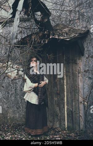 Une femme se tient près d'un mur sale avec une vieille porte. Fille dans une robe vintage pour une fête d'Halloween Banque D'Images