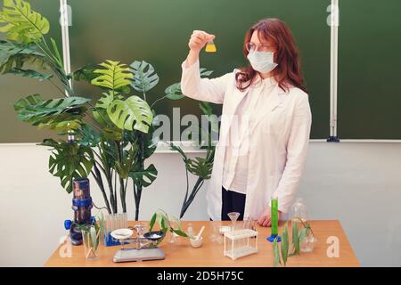 Femme mignonne enseignante dans un masque médical mène une leçon de chimie. L'éducation pendant l'épidémie du coronavirus et l'apprentissage à distance à l'école Banque D'Images