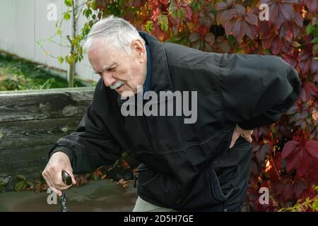 Un homme âgé aux cheveux gris souffrant de douleurs dorsales. Un vieil homme tient sa douleur en arrière comme il se tient debout de la banquette Banque D'Images