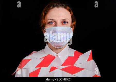 Femme attachée dans une chemise blanche et un masque médical sur fond noir. Concept de personnes isolées dans une quarantaine de coronavirus Banque D'Images