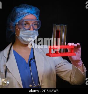 Une infirmière en lunettes de protection et un masque médical avec des tubes à essai sur pied dans sa main. Un médecin muni d'un stéthoscope tient des flacons de tests sanguins sur un support Banque D'Images