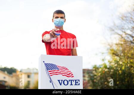 Homme avec masque de visage montrant j'ai voté aujourd'hui badge à l'urne. Banque D'Images