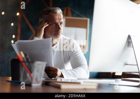 Homme d'affaires décontracté aux cheveux gris regardant à travers des documents papier. Le responsable comptable de sexe masculin examine le rapport financier Banque D'Images