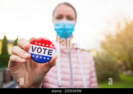 Femme avec masque de visage montrant le bouton de vote aux élections américaines à l'extérieur. Banque D'Images