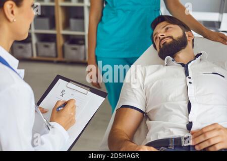 Patient mâle allongé sur le lit d'hôpital dans le bureau du médecin à l'écoute aux conseils de santé du clinicien Banque D'Images