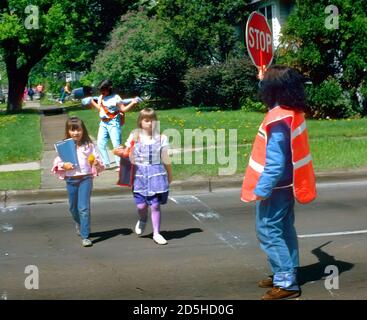 Crossing Guard femelle les élèves du primaire permet de traverser une rue animée par la tenue d'un signe de la circulation d'arrêt Banque D'Images