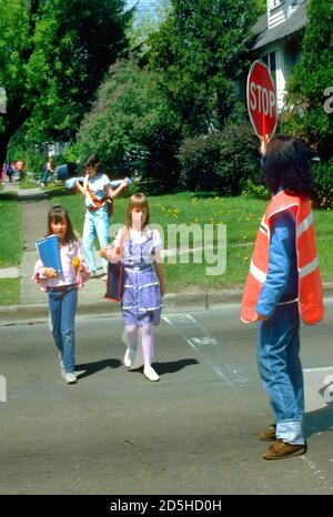 Crossing Guard femelle les élèves du primaire permet de traverser une rue animée par la tenue d'un signe de la circulation d'arrêt Banque D'Images