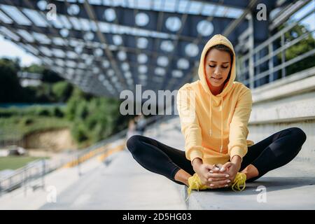 Femme mince à capuche jaune qui étire les jambes sur les marches Banque D'Images
