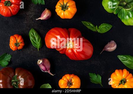 Composition de tomates en tomates biologiques colorées, basilic, ail sur fond noir. Vue du dessus. plat. Concept de cuisine alimentaire végétalienne Banque D'Images