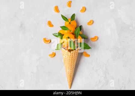 Fruits mandarine orange ou mandarine au cornet de glace gaufrée avec tranches sur fond de béton. Concept de la nourriture de Noël en hiver. Vue du dessus. plat Banque D'Images