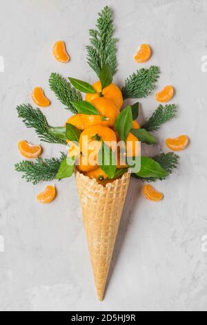Fruits orange mandarine en cône de glace gaufré avec tranches et branches de sapin sur fond de béton. Concept de la nourriture de Noël en hiver. Vue du dessus. fla Banque D'Images