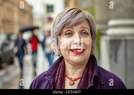 Femme européenne d'âge moyen souriante dans une rue bondée d'une grande ville par temps pluvieux, en gros plan. Banque D'Images