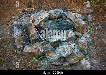 Un grill impromptu fait de pierres dans une forêt avec des charbons éteints. Banque D'Images