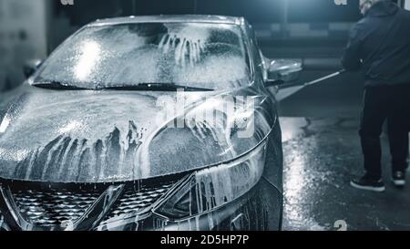 Lavage de voiture la nuit. Homme nettoyant sa voiture en utilisant de l'eau haute pression en libre-service. Banque D'Images