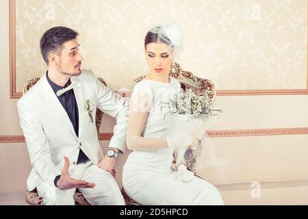 Jeune mariée et marié en colère, homme et femme se sont bouleversés les uns sur les autres assis dans des fauteuils regardant le côté isolé sur fond classique. Conflit entre les deux Banque D'Images