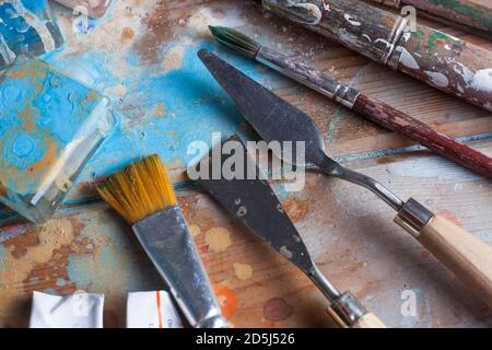 Bureau d'artiste et matériel. Divers pinceaux et couteaux à palettes. Le bureau en bois est recouvert de belles peintures de différentes couleurs. Banque D'Images