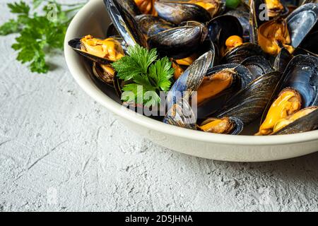 Délicieuses moules fraîches cuites à la vapeur dans une sauce au vin blanc avec persil dans une plaque blanche sur un fond gris gros plan Banque D'Images