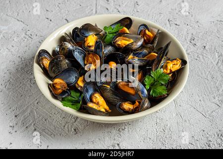 Délicieuses moules fraîches cuites à la vapeur dans une sauce au vin blanc avec persil dans une plaque blanche sur fond gris Banque D'Images