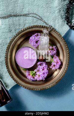 Fleurs de verveine pourpre avec une bougie aromatique et un flacon de parfum, grenaille sur fond bleu Banque D'Images