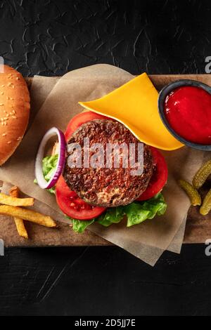 Hamburger avec du bœuf, du fromage, de l'oignon, de la tomate et de la salade verte, avec un petit pain et du ketchup, avec des frites, avec une photo en hauteur et un espace pour le texte Banque D'Images