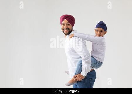 UN PÈRE SIKH PORTANT SON FILS DANS LE DOS ET SOURIANT HEUREUSEMENT Banque D'Images