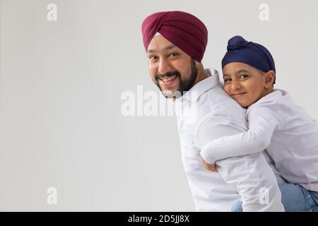 UN PETIT SIKH GARÇON EMBRASSANT SON PÈRE HEUREUX ET REGARDANT À L'APPAREIL PHOTO Banque D'Images