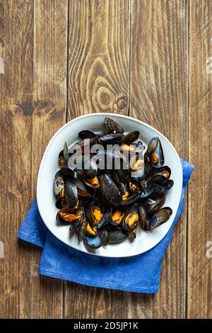 Délicieuses moules fraîches cuites à la vapeur dans une sauce au vin blanc avec persil dans une plaque blanche sur une table en bois Banque D'Images