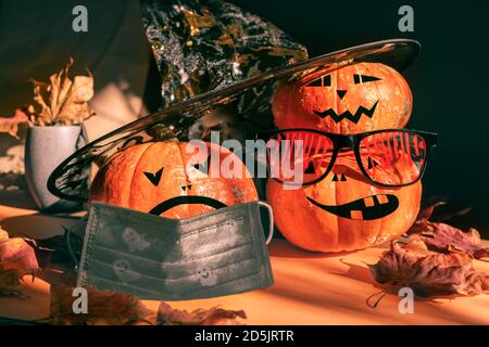 Trois citrouilles d'halloween peintes comme lanterne de Jack dans des verres sanglants de fête, un chapeau, un masque facial avec des feuilles et des ombres. Banque D'Images