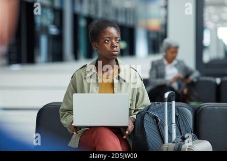 Jeune femme africaine utilisant son ordinateur portable tout en étant assise et en attente de son vol à l'aéroport Banque D'Images