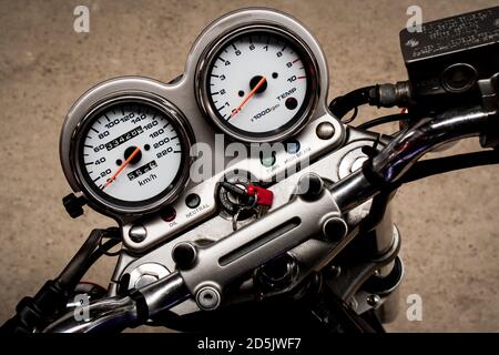 Le compteur de vitesse à flèche d'une moto sur le volant qui se trouve sur un gros plan de route en béton. Tableau de bord coloré d'une moto sport, vue du dessus. Horiz Banque D'Images