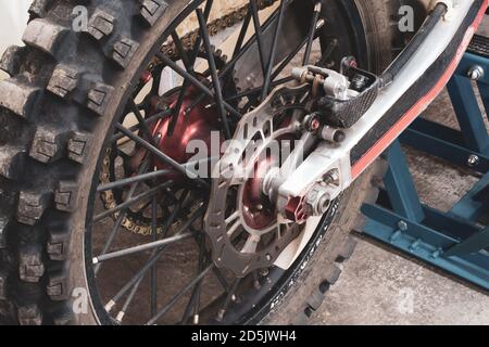 Gros plan sur la roue arrière cloutée d'une moto hors route endoro dans le garage sur l'ascenseur. Disques de frein, chaîne, transmission. La photo d'une partie de vélo a été prise Banque D'Images